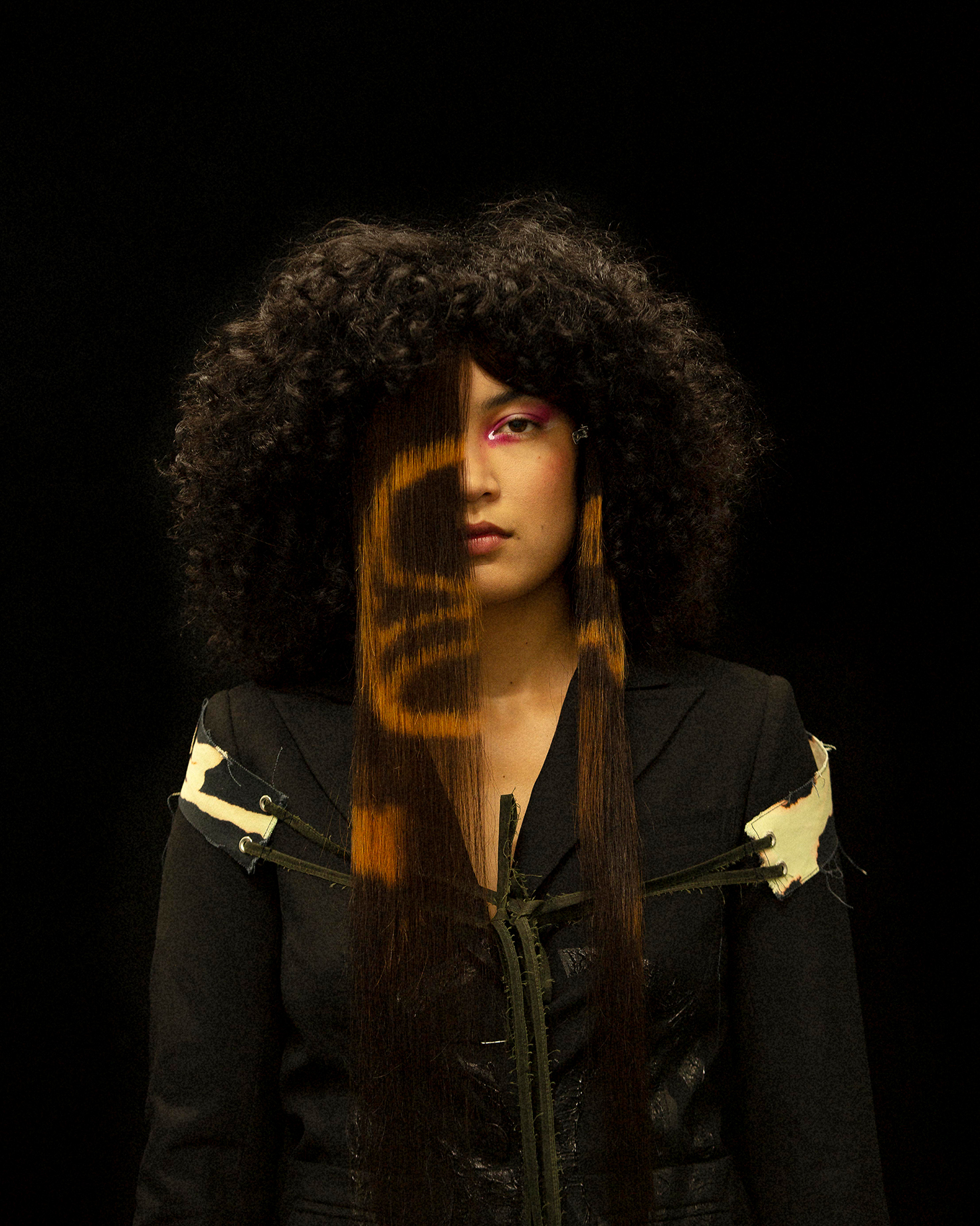 Portrait shot of a model facing the camera against a black background, half of her face is covered in long straight hair